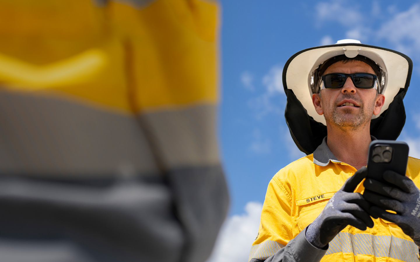 Uma pessoa da equipe de campo vestindo equipamento de proteção segura um iPhone enquanto conversa com alguém