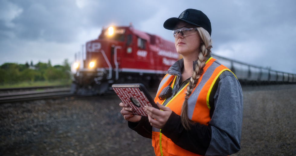 Uma funcionária da ferrovia segura um iPad e observa os trilhos enquanto um trem passa